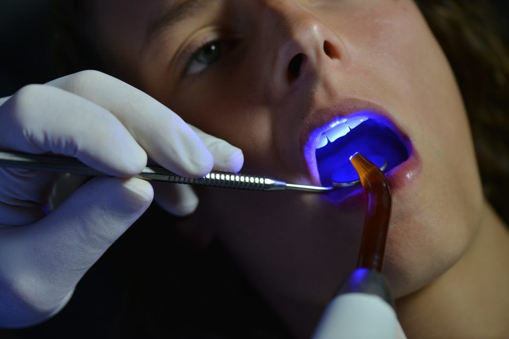 Man having a dental exam with a blue light in his mouth
